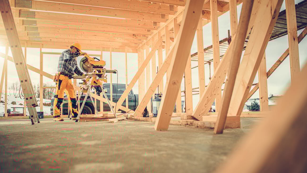 Caucasian Contractor Carpenter Worker in His 40s Using Commercial Grade Circular Saw in Construction Zone. Industrial Theme. Wooden Skeleton Framing Building.; Shutterstock ID 1907699314
