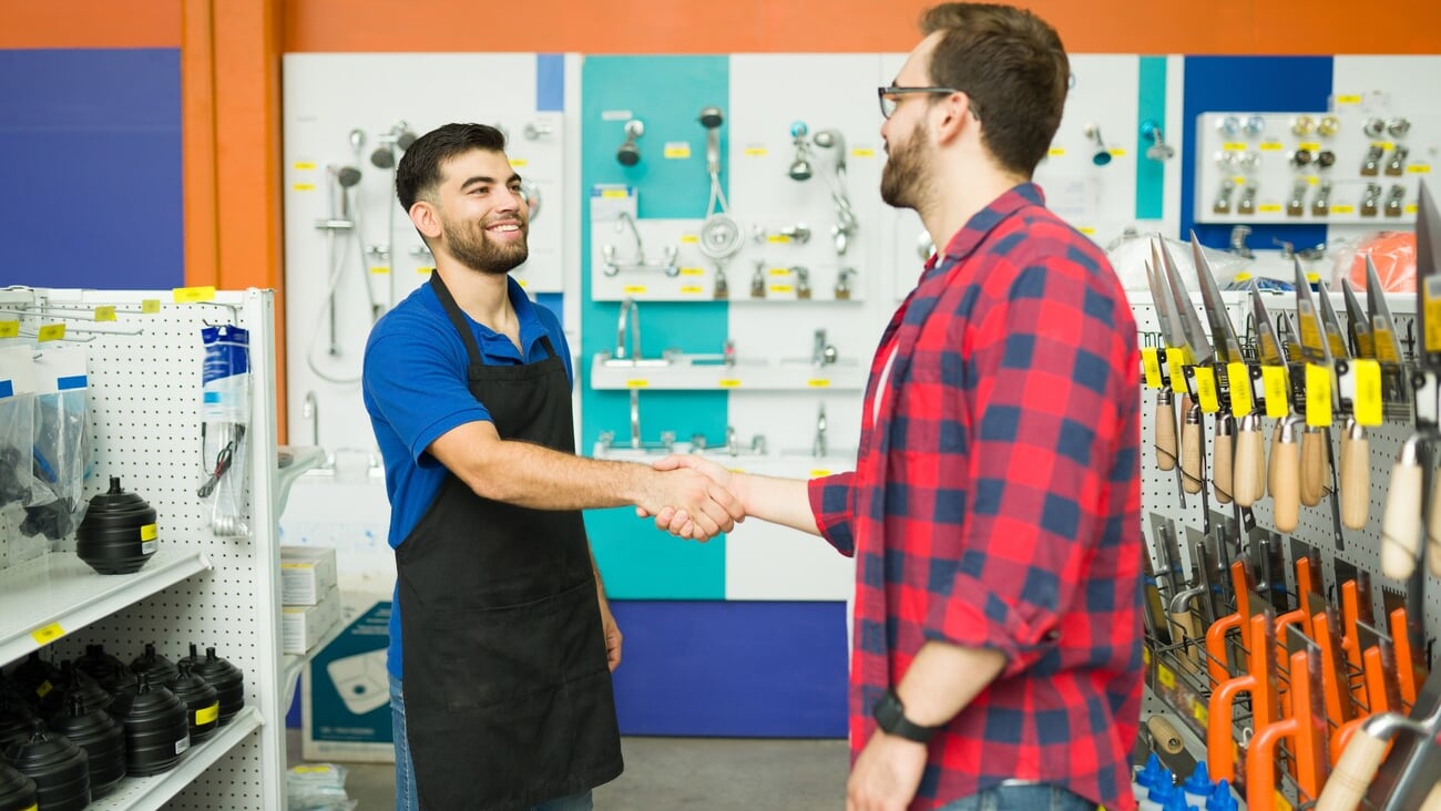 Cheerful male employee smiling shaking hands with a young man and greeting him to the hardware store during his shopping; Shutterstock ID 2193305875