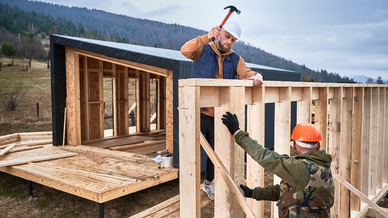 Man worker building wooden frame house on pile foundation. Carpenter hammering nail into wooden joist, using hammer. Carpentry concept.; Shutterstock ID 2356031675