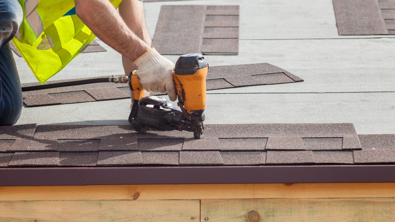 Construction worker putting the asphalt roofing (shingles) with nail gun on a new frame house; Shutterstock ID 416537164