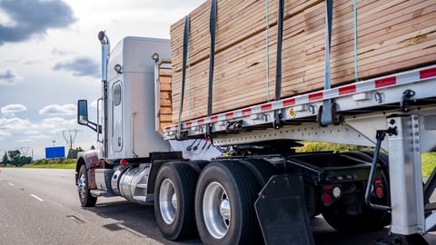 White classic powerful bonnet American big rig professional semi truck tractor transporting tightened wood lumber cargo on flat bed semi trailer running on wide multiline highway road; Shutterstock ID 1846308355
