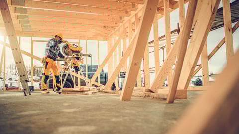 Caucasian Contractor Carpenter Worker in His 40s Using Commercial Grade Circular Saw in Construction Zone. Industrial Theme. Wooden Skeleton Framing Building.; Shutterstock ID 1907699314