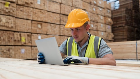 Male warehouse worker wearing uniform working with labtop computer in wooden warehouse storage; Shutterstock ID 2355623905