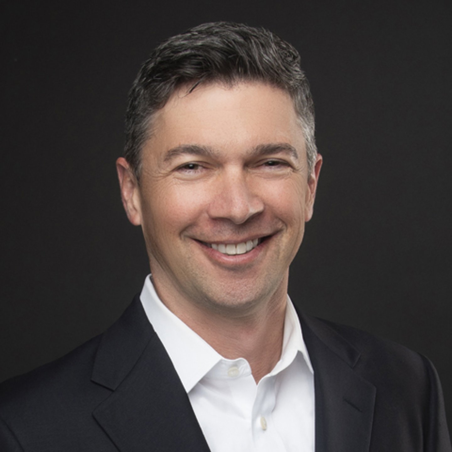 a man wearing a suit and tie smiling at the camera