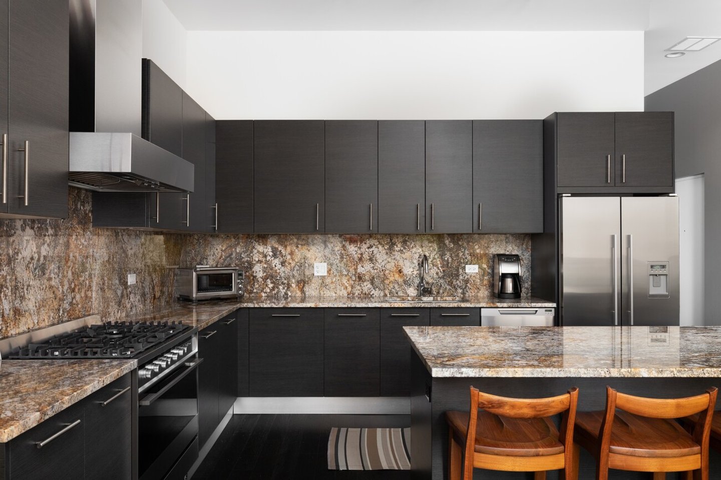 CHICAGO, IL, USA - JUNE 28, 2021: A modern kitchen with brown cabinets, granite countertops, bar stools sitting at the large island, and Fisher  Paykel stainless steel appliances.; Shutterstock ID 2172502733