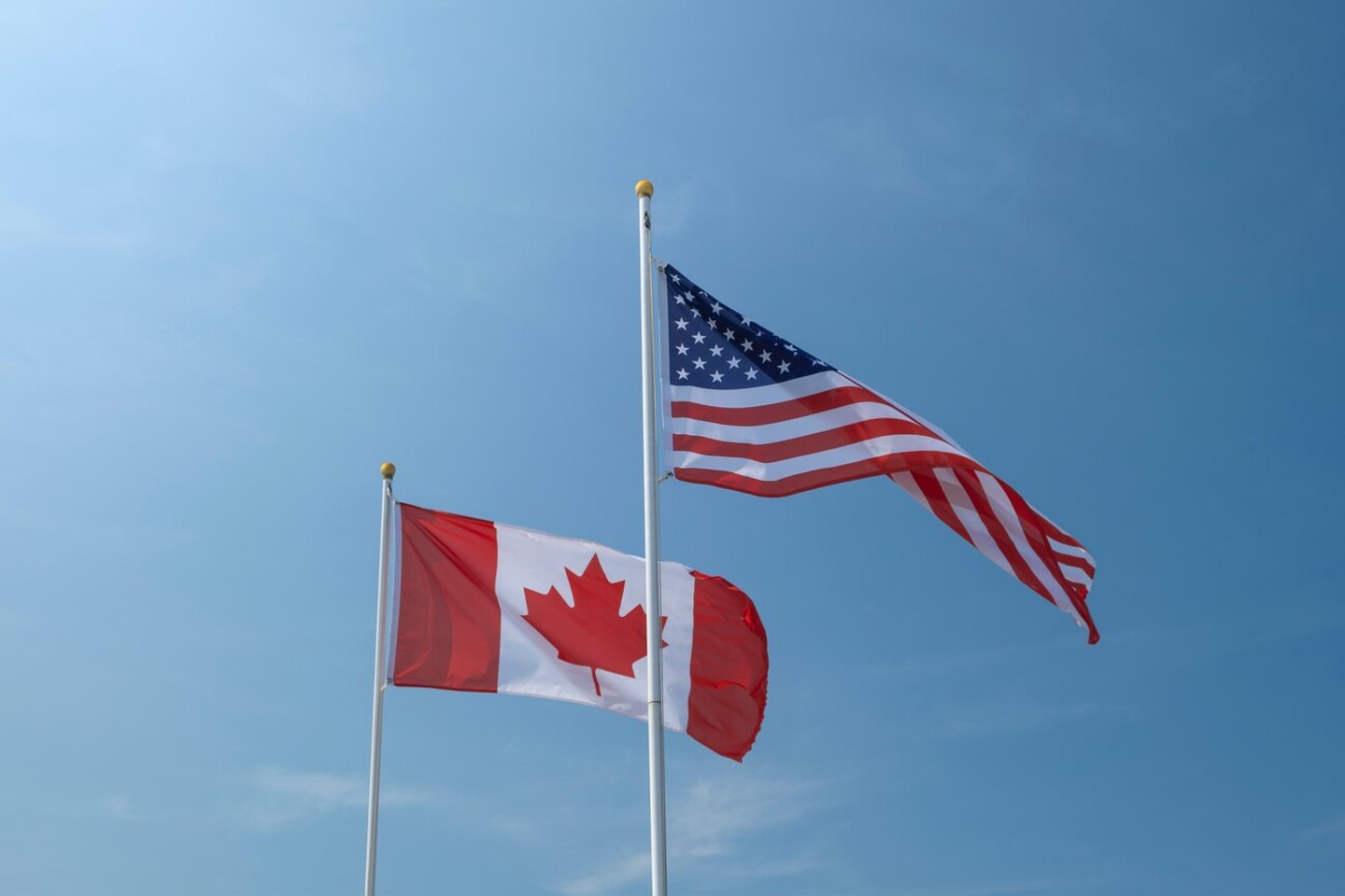 USA and Canadian flags waving left to right against blue sky. Economy, politics, partnership, external affairs concept.; Shutterstock ID 2395461801