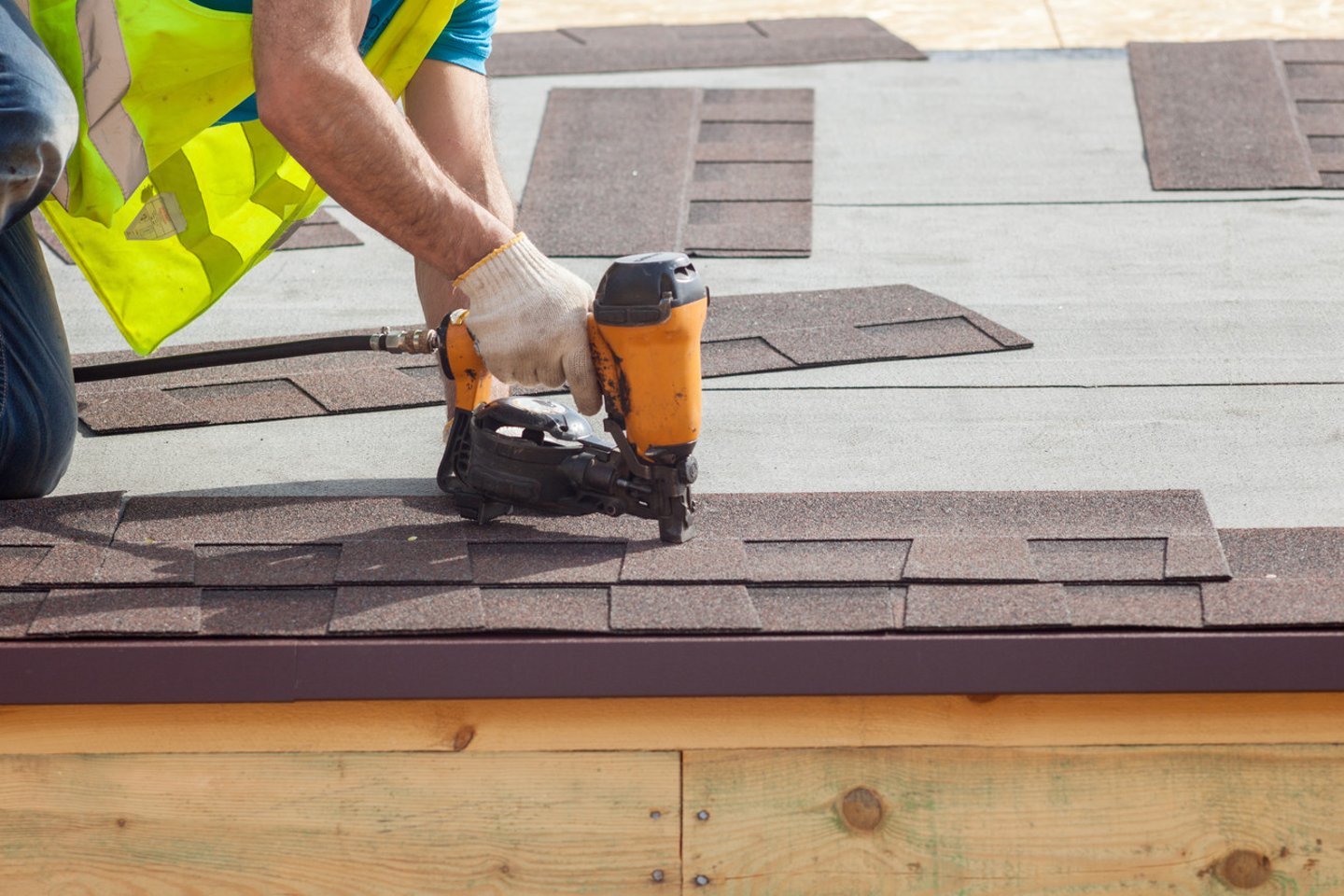 Construction worker putting the asphalt roofing (shingles) with nail gun on a new frame house; Shutterstock ID 416537164