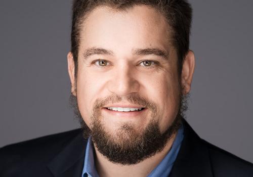 a man wearing a suit and tie smiling and looking at the camera