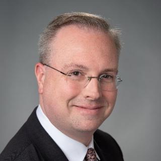 Robert Dietz wearing a suit and tie smiling and looking at the camera
